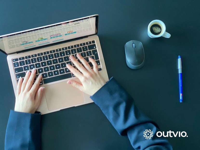 Zbliżenie na ręce sprzedawcy internetowego który chce sprzedawać z Polski za granicą na stole znajduje się espresso w filiżance, laptop z otwartym CMS oraz niebieski długopis myszka a biznesman ubrany jest w marynarkę